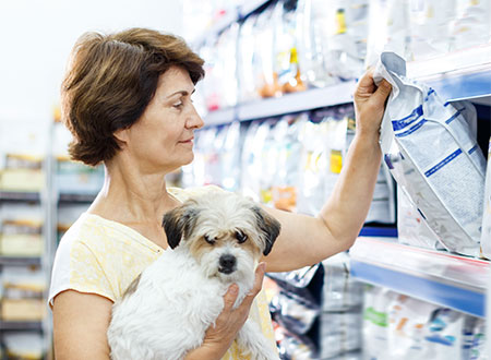 woman holding her dog while grabbing pet food bag off of shelf